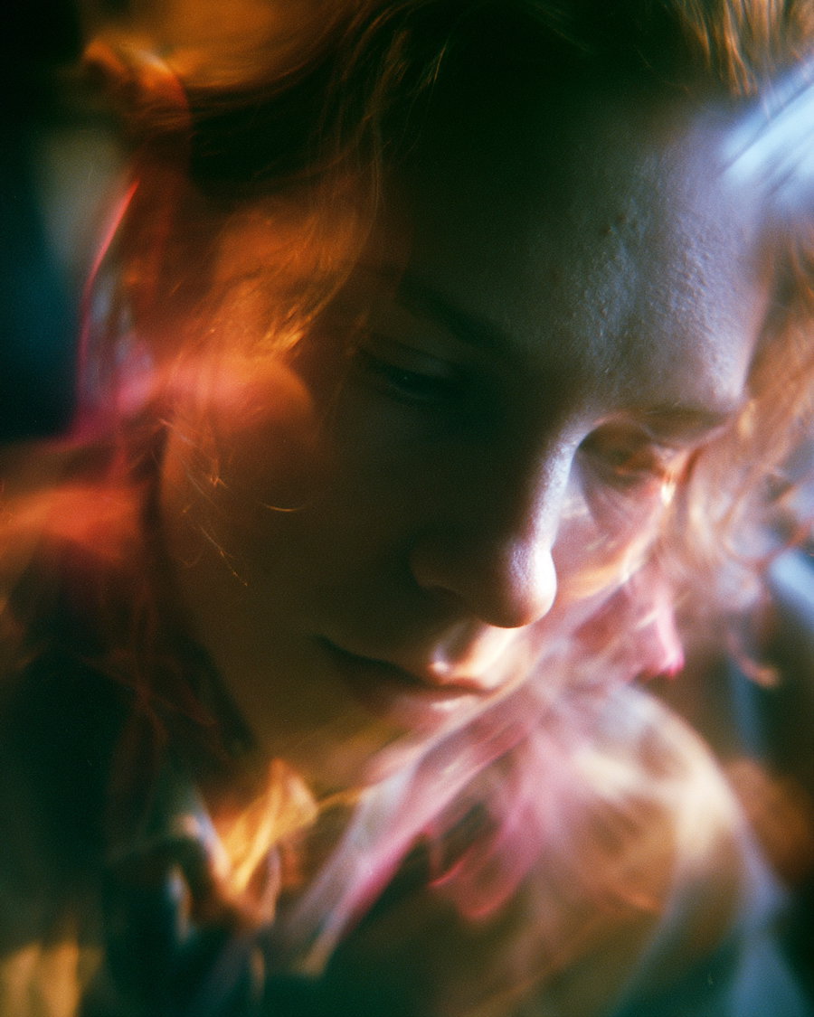 Portrait of a person with reddish hair, softly blurred with colorful light reflections and shadows creating a dreamy atmosphere