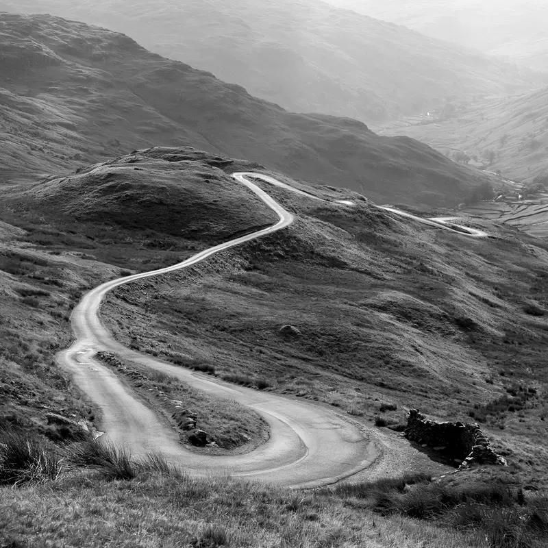 Monochrome photograph capturing a winding road through hilly terrain