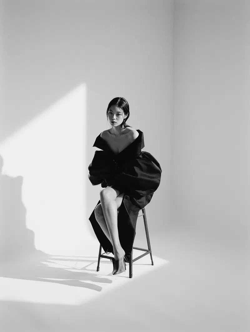 Black and white artistic portrait of a woman in black fashion attire sitting on a stool
