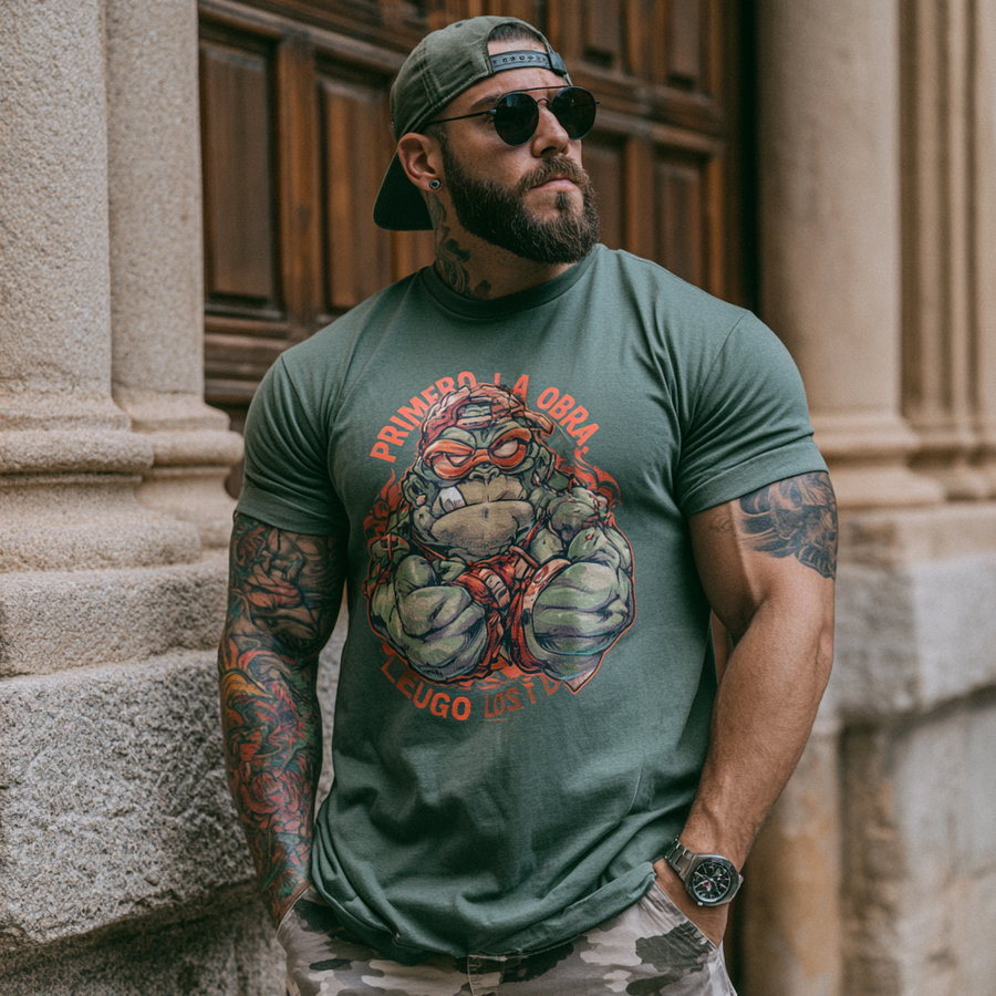 A muscular man with a beard, sunglasses, and a backwards cap wearing a green t-shirt with a colorful cartoon turtle and Spanish text, standing against a stone wall and wooden door.