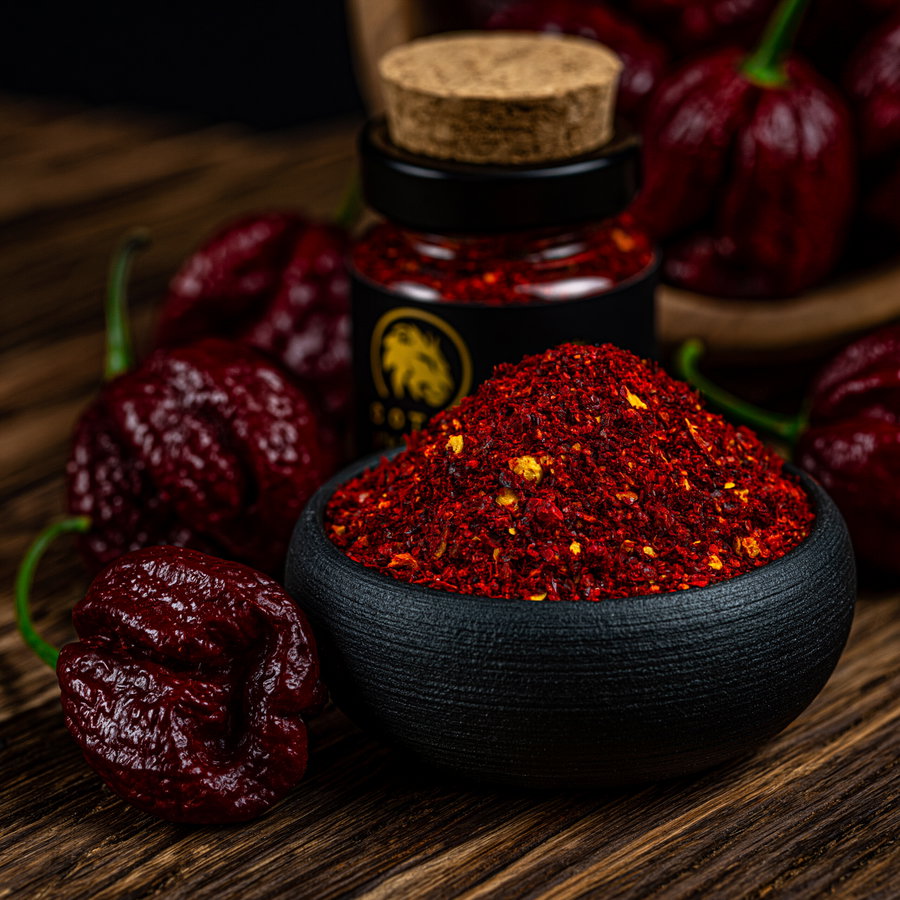 Close-up photo showing dried wrinkled red chili peppers and a black bowl filled with red chili powder on a wooden surface with a jar in the background