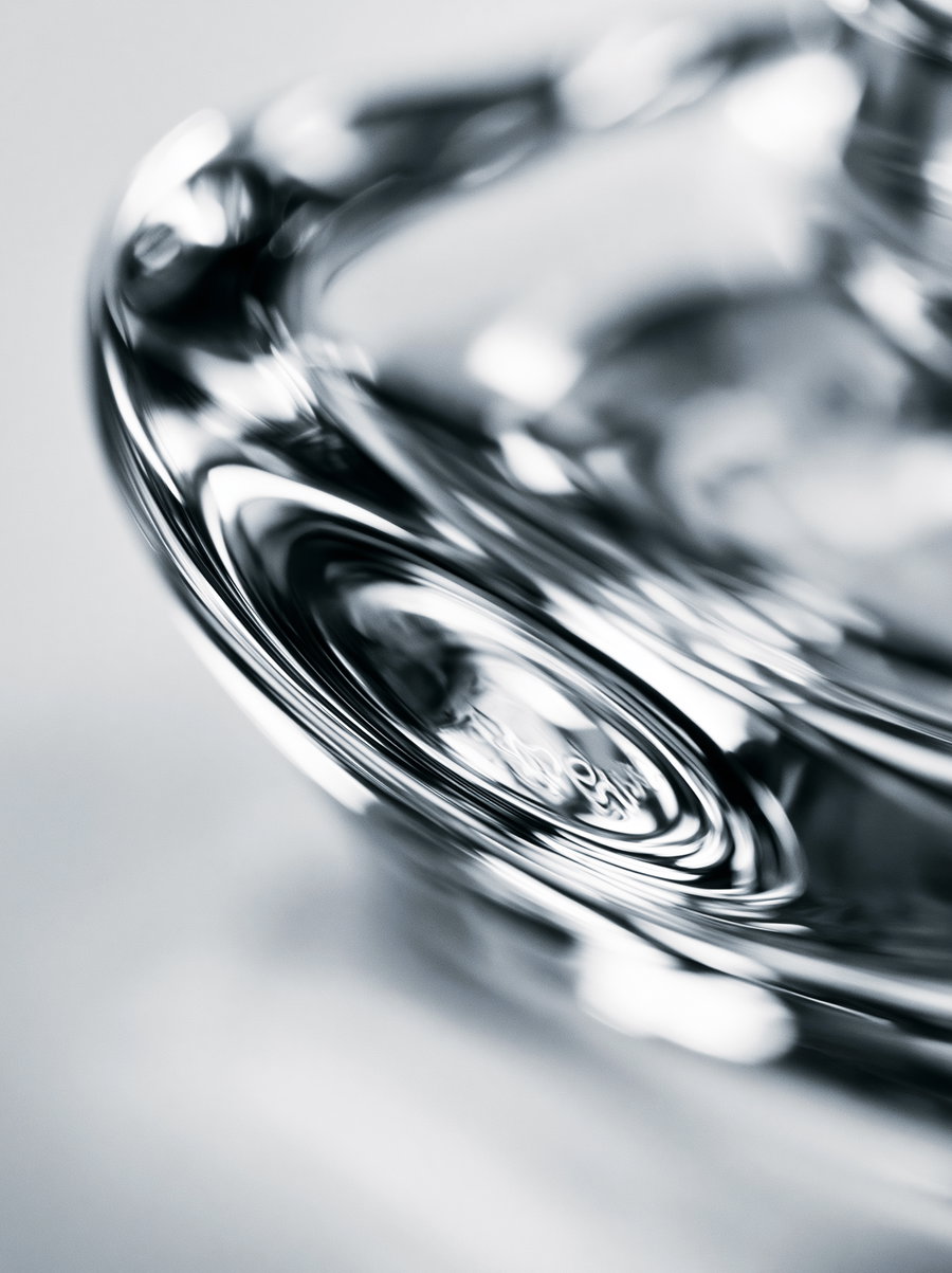 A close-up black and white image showing reflective, smooth, and distorted surfaces of a glass-like object with abstract shapes and light reflections
