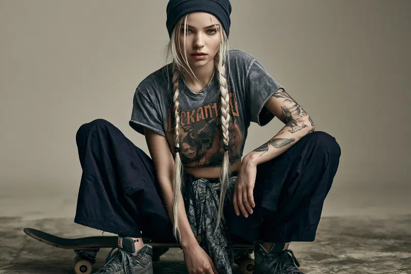 Artistic portrait of a young woman with braided hair and tattoos sitting on a skateboard