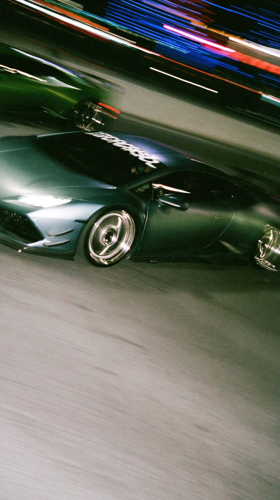 Blurred image of a dark sports car speeding on a road at night with streaking lights in the background