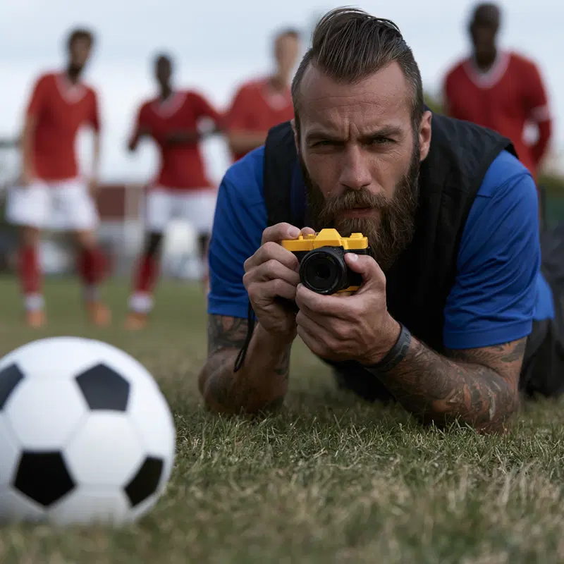 Photographer capturing a soccer ball with players in the background