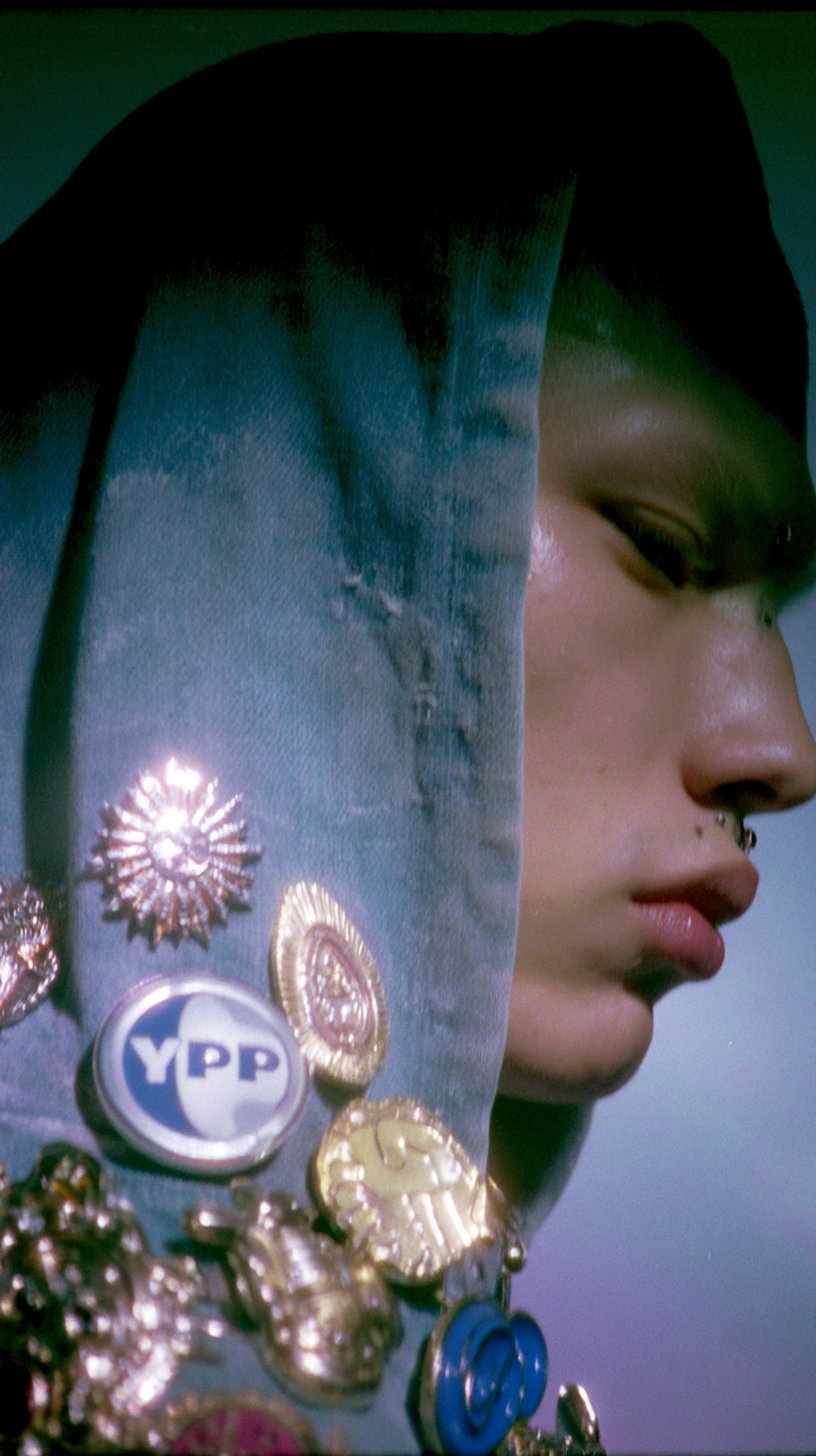 Side profile of a person wearing a hood adorned with various shiny pins and brooches