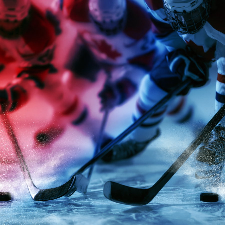 Close-up image of ice hockey players in protective gear with sticks and pucks on the ice, illuminated with red and blue lights
