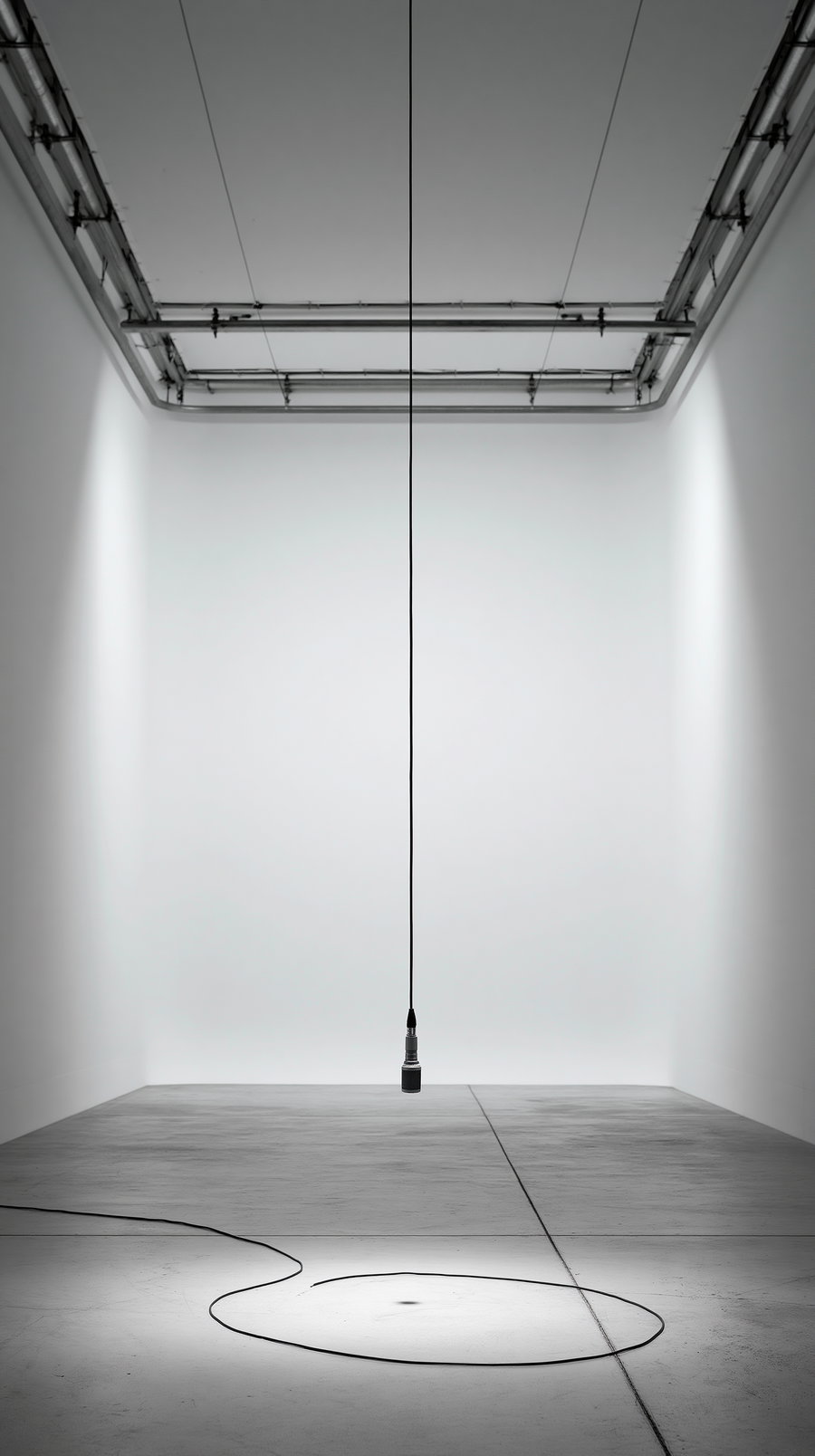 a black microphone hanging from the ceiling by a cable in a white, empty gallery space with concrete floor and spotlight illuminating the floor forming a circular pattern