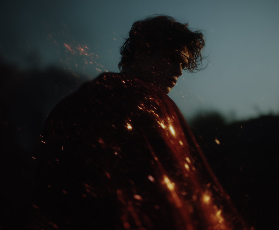 A moody, artistic portrait of a person covered in glowing embers with a dark background and a dusky sky.