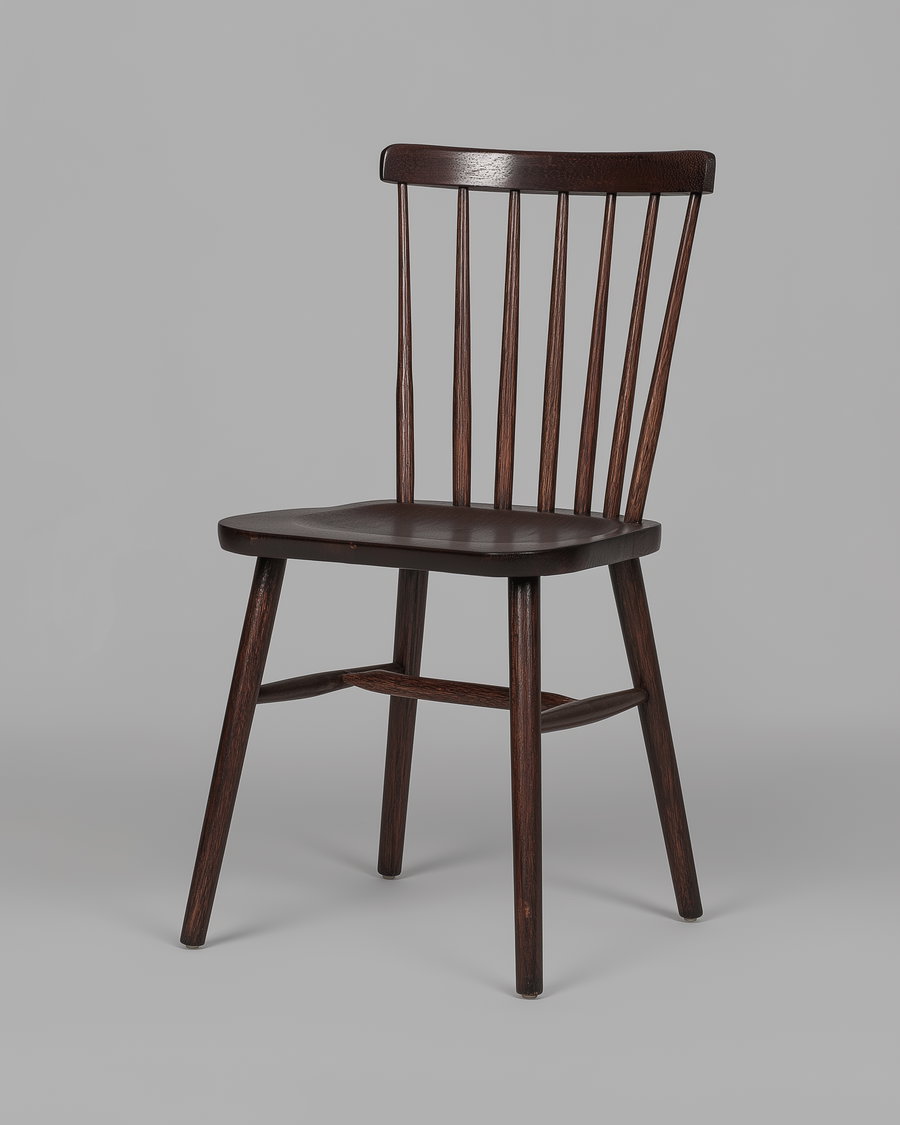 A dark wooden chair with a curved vertical spindle backrest and four tapered legs against a plain gray background.