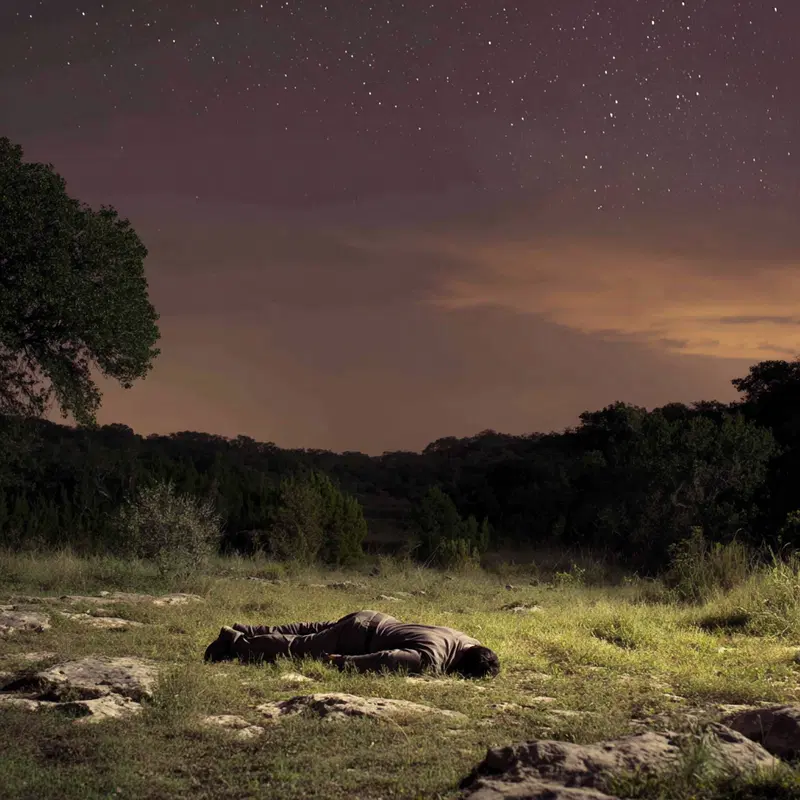Man lying on grassy landscape under a starry night sky with moody lighting