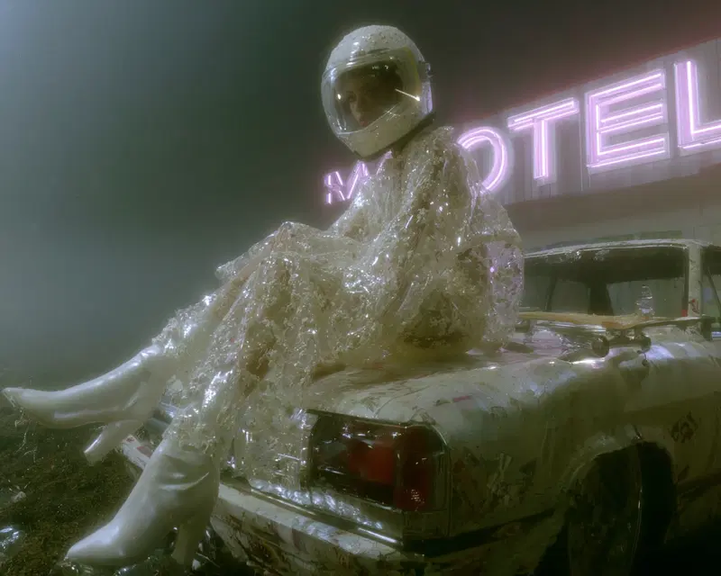 Surreal aesthetic photo of person in futuristic outfit sitting on vintage car in fog