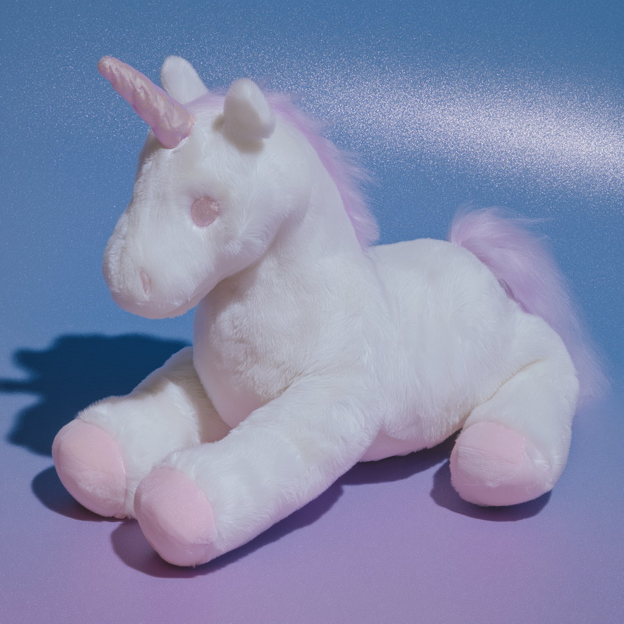 Plush unicorn stuffed toy in white and pink lying on a gradient blue to purple surface with a soft shadow