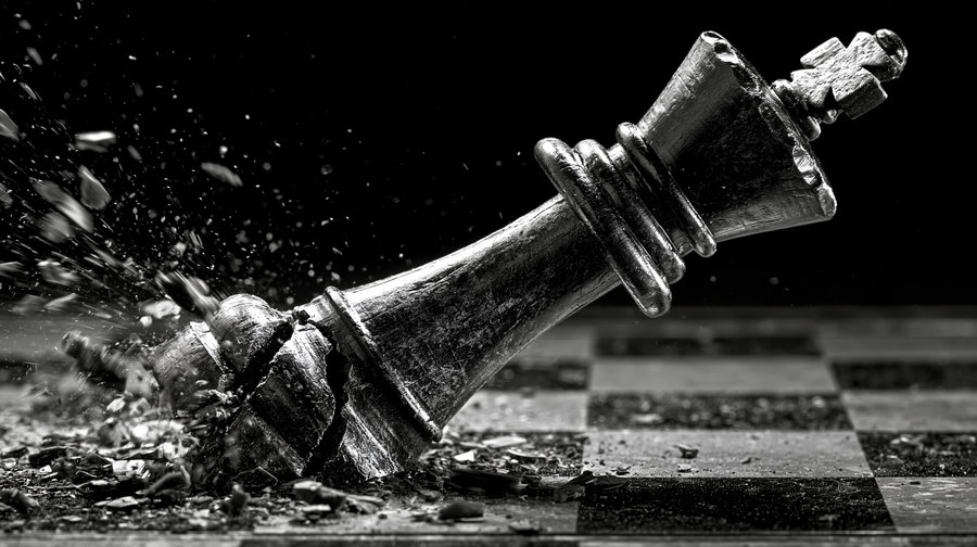 Close-up of a shattered black chess king piece falling on a chessboard with chips and dust flying