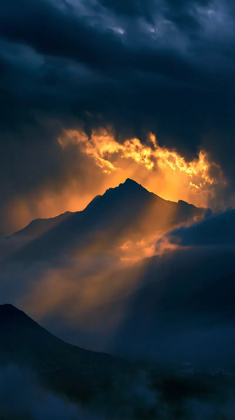 Dramatic mountain silhouette with golden sunlight breaking through dark storm clouds