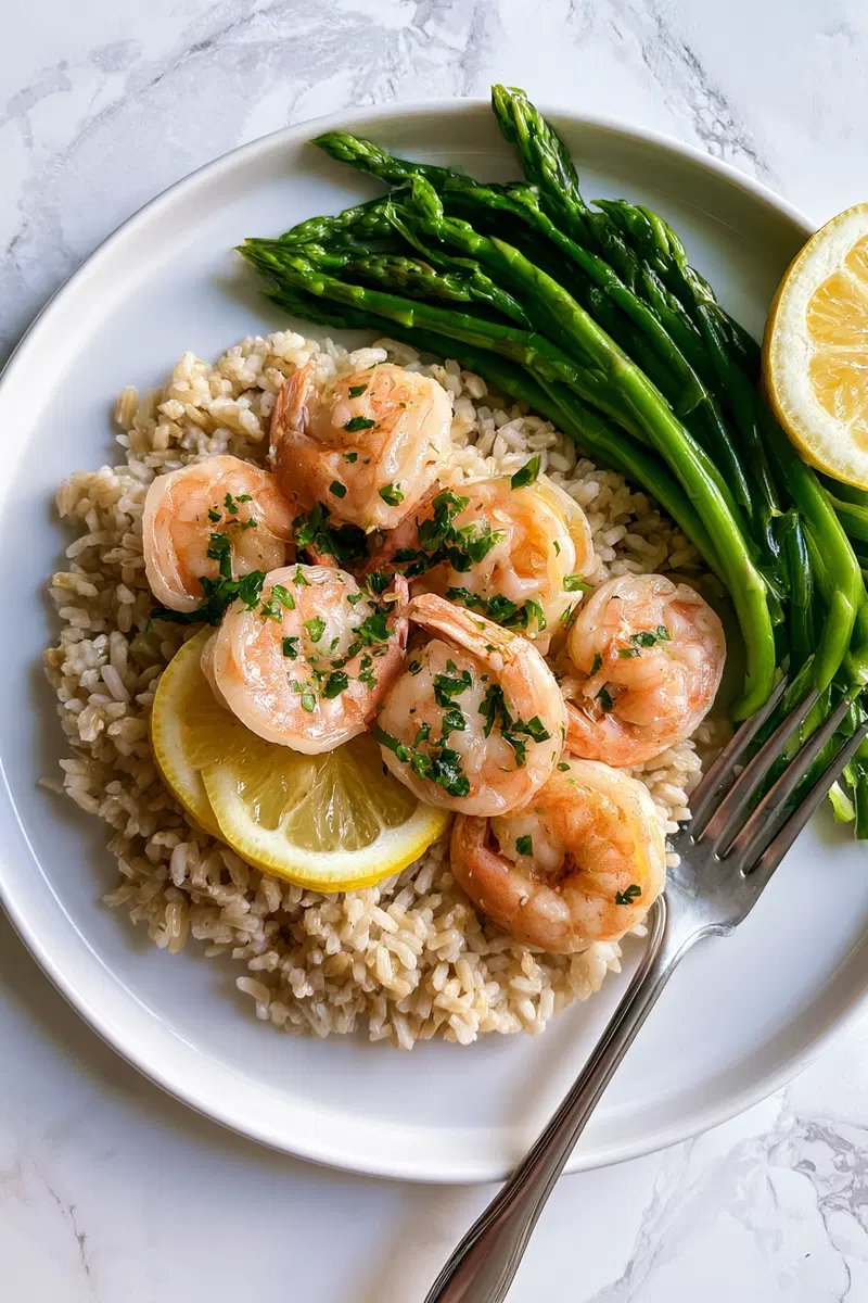 Freshly cooked shrimp with lemon slices, asparagus, and rice on a white plate