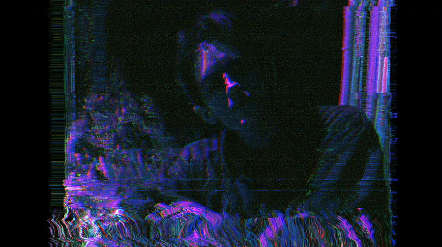 A distorted and glitchy portrait of a person in dark surroundings with intense purple and blue color effects and noise.