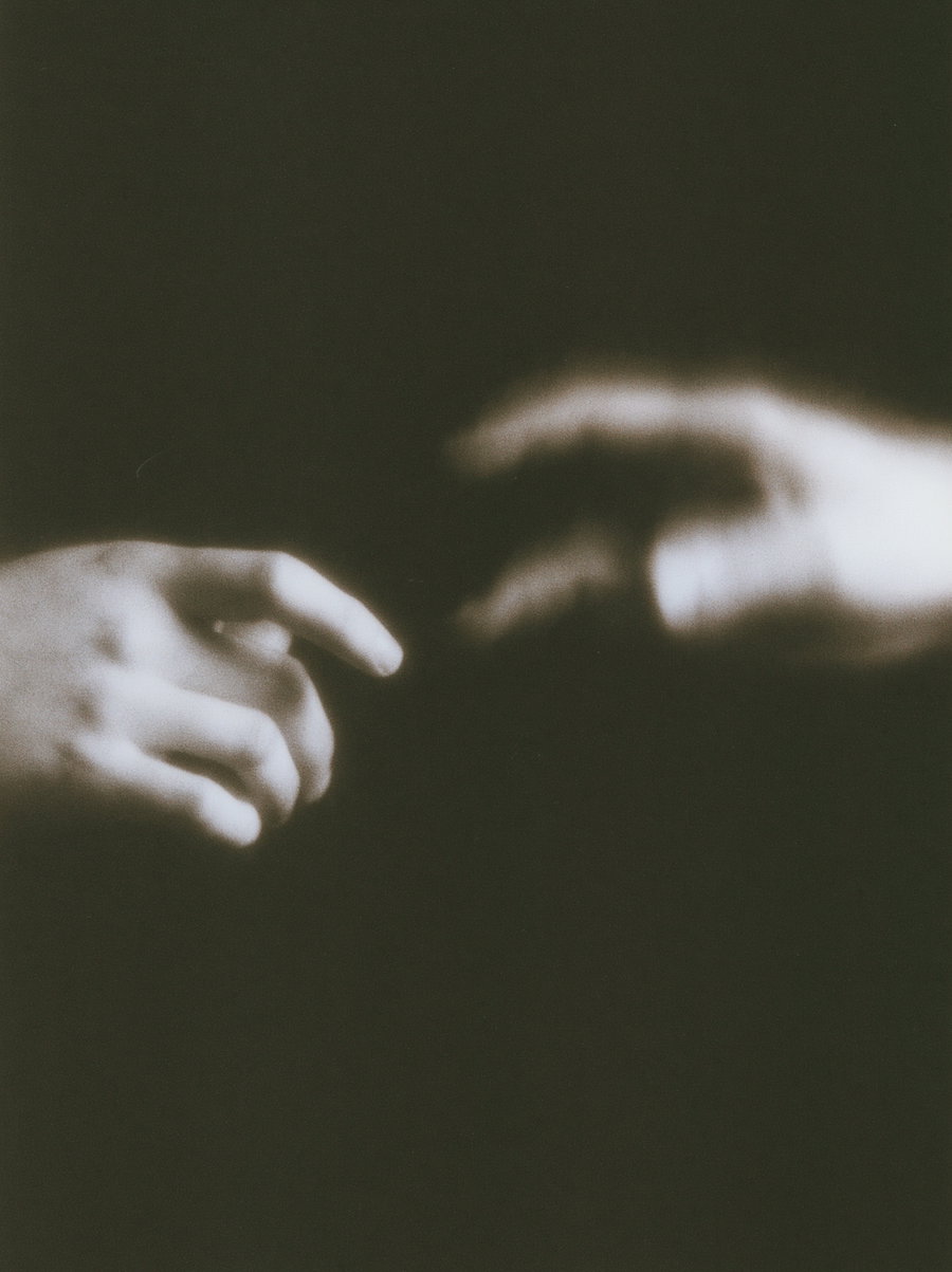 Black and white photo showing two hands reaching toward each other with a blurred effect on a black background