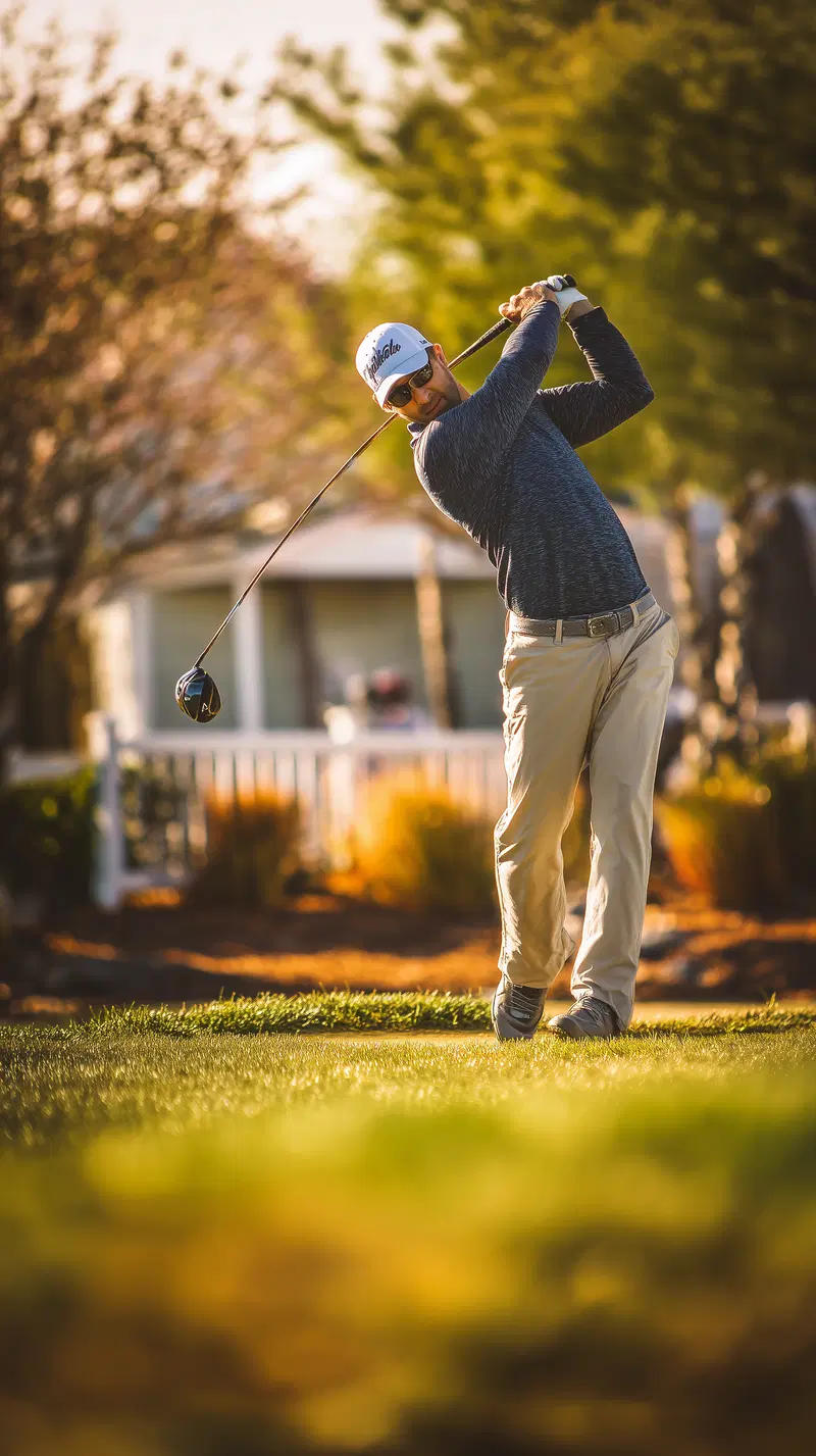 Golfer in mid-swing on a sunny day at the golf course with blurred background