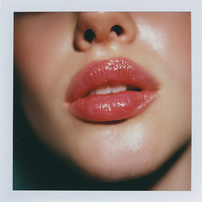 Close-up portrait of glossy lips and part of the nose in soft lighting