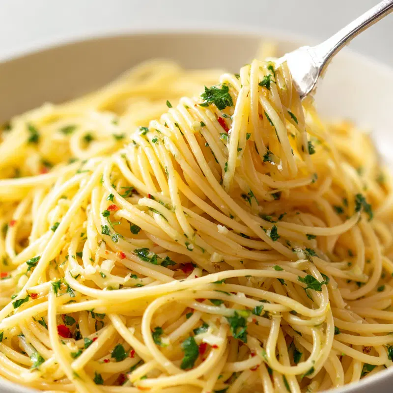 Close-up of spaghetti aglio e olio with herbs and chili flakes on a fork