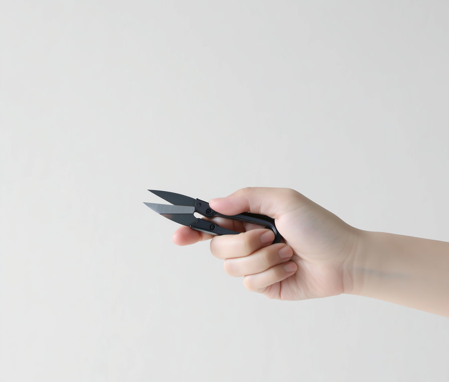 A human hand holding black scissors with short blades against a plain light background