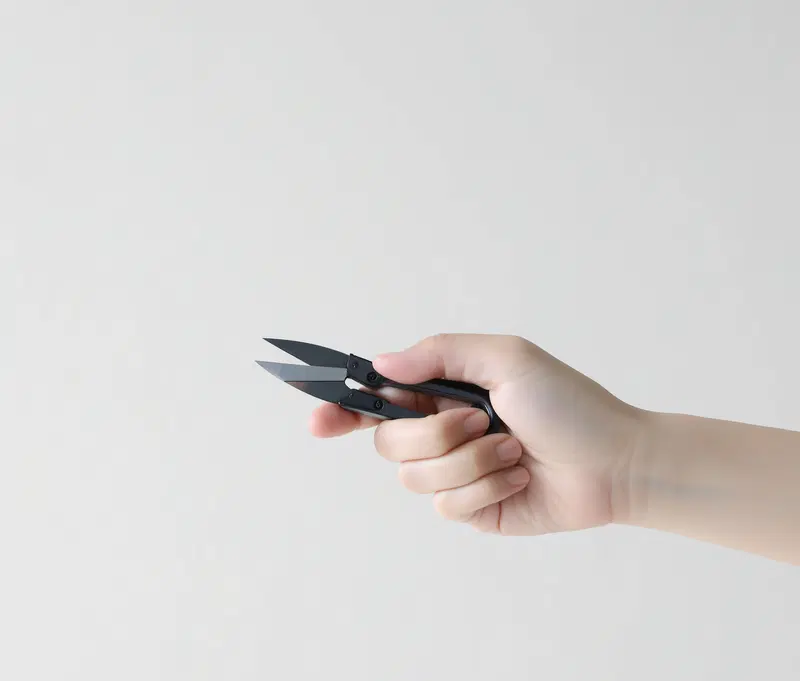 Close-up of a hand holding a pair of small black scissors on white background