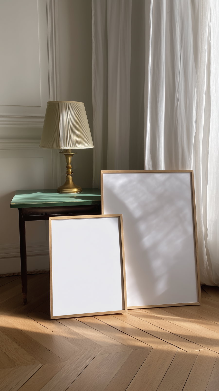 Two empty wooden picture frames leaning on a wooden floor next to a green table with a vintage brass lamp, with white curtains in the background