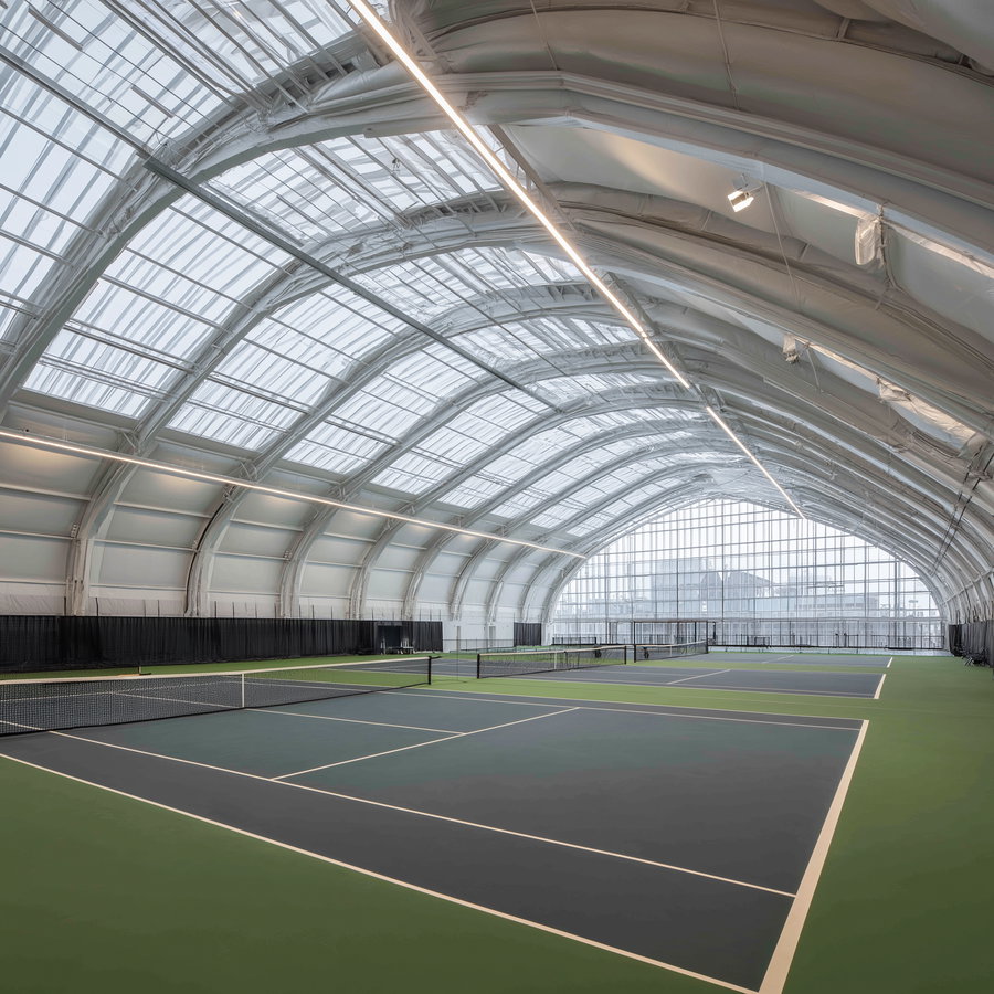 Modern indoor tennis courts with green and blue surfaces under a large curved glass and metal canopy