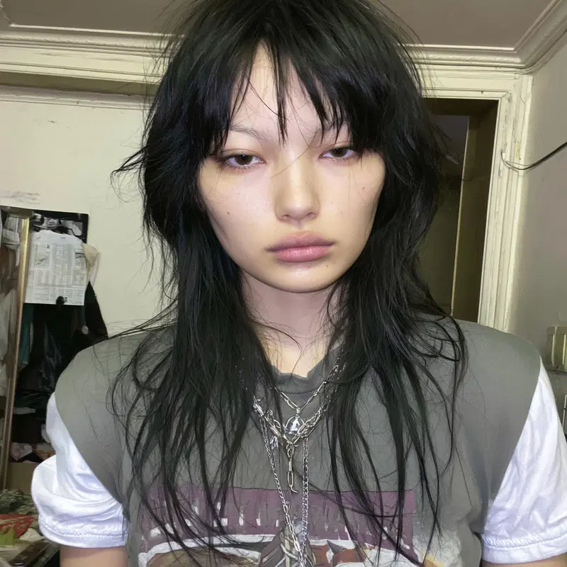 Close-up portrait of a person with long black hair and layered necklaces in casual attire