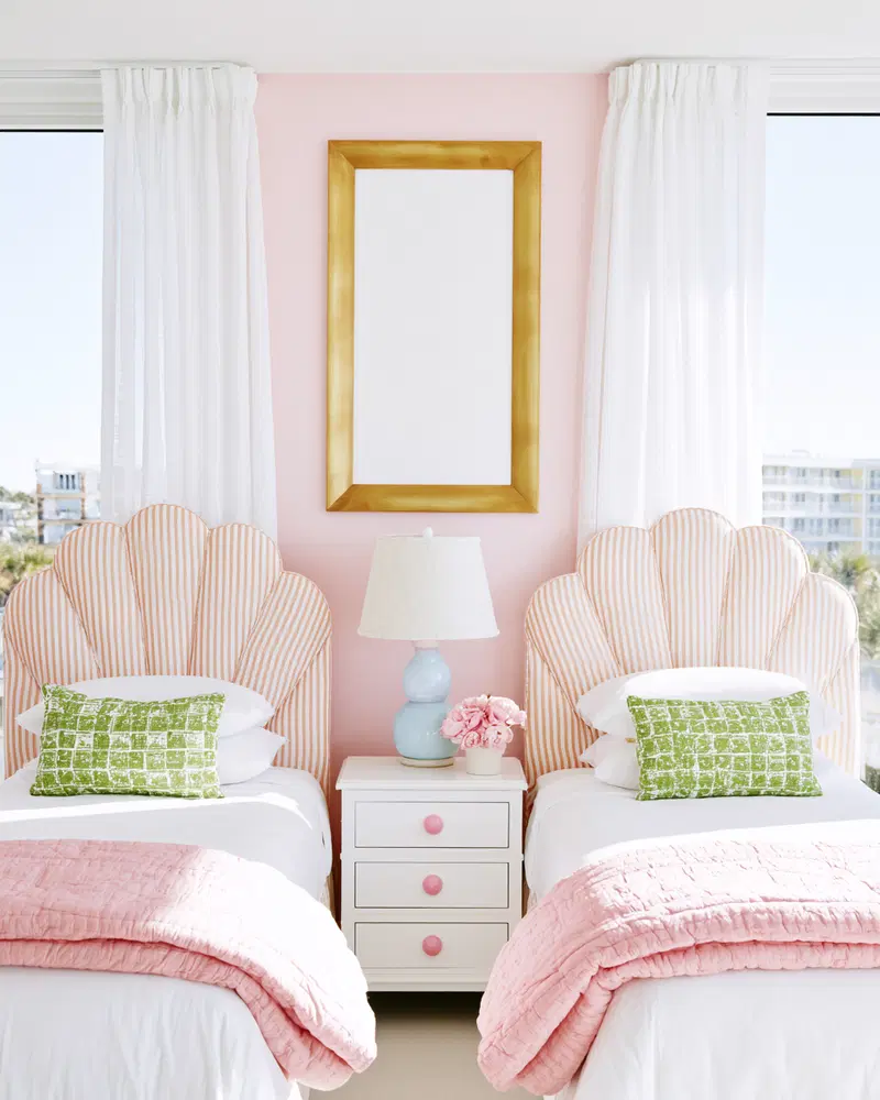 Pastel pink bedroom with twin beds featuring striped headboards and green pillows