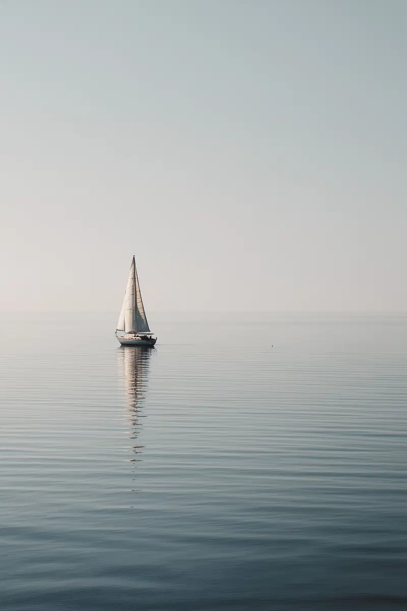Serene sailboat on calm ocean water with soft blue sky