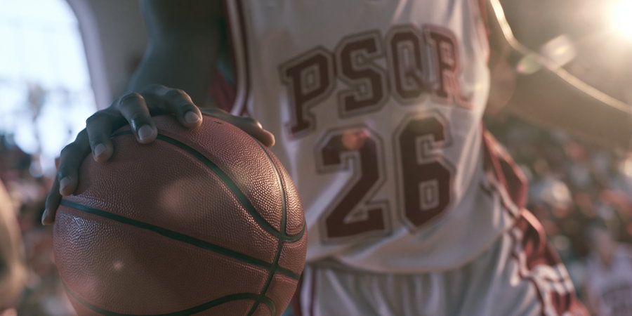 A close-up of a basketball player holding a basketball with a crowded outdoor background in soft sunlight