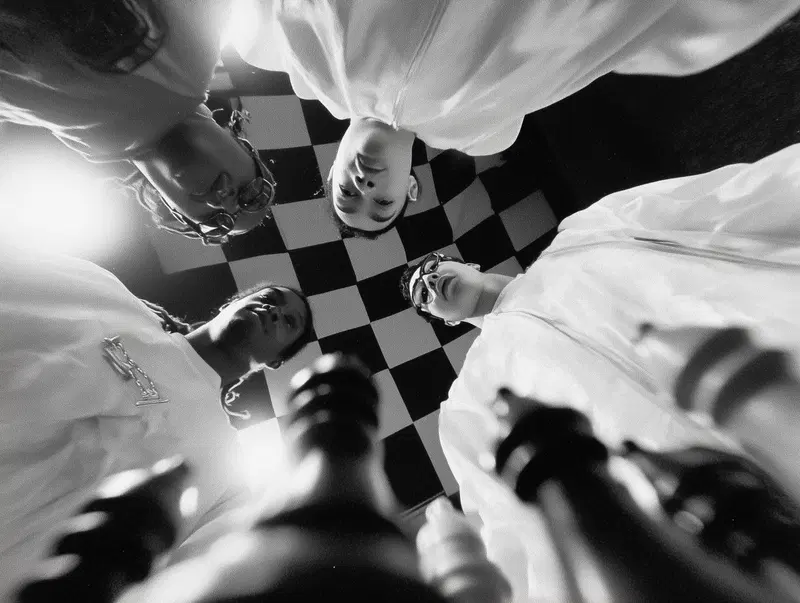 Black and white photo of four people in white coats standing over a chessboard