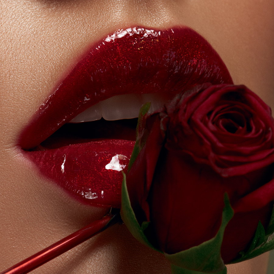 Extreme close-up of glossy red lips holding a fresh red rose near mouth
