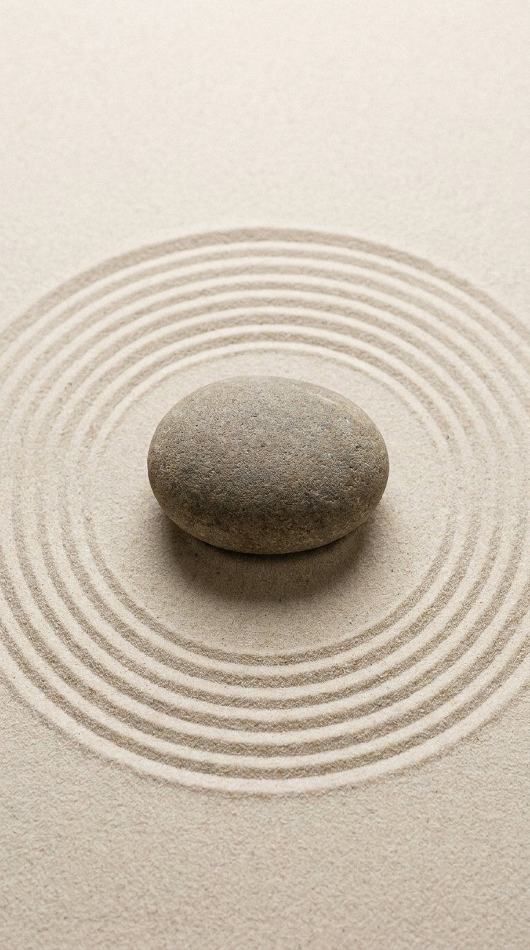 A smooth grey stone placed on sand with evenly spaced concentric circles drawn around it