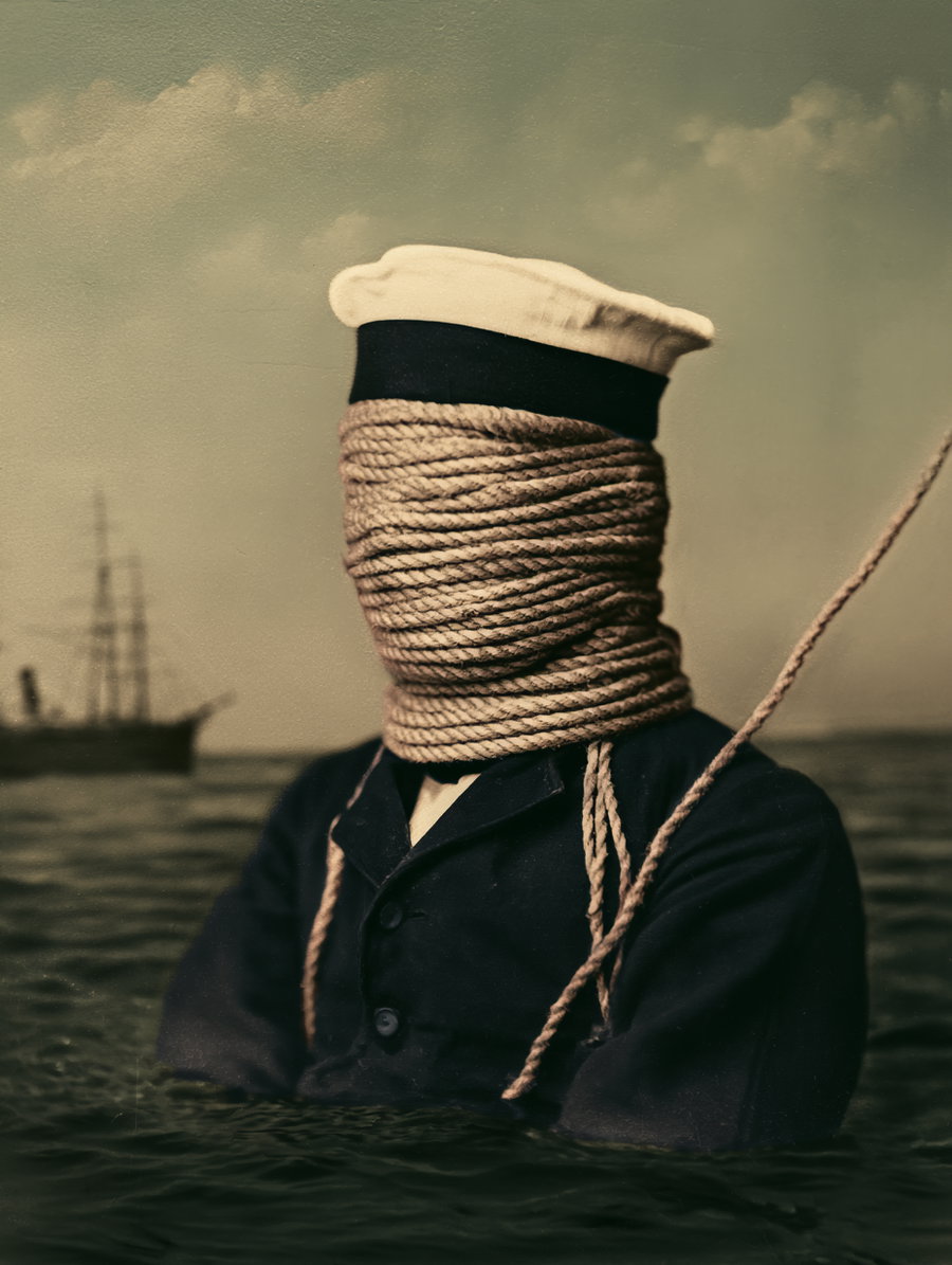 A sailor's head is completely wrapped in rope, standing in water with a ship visible in the background.