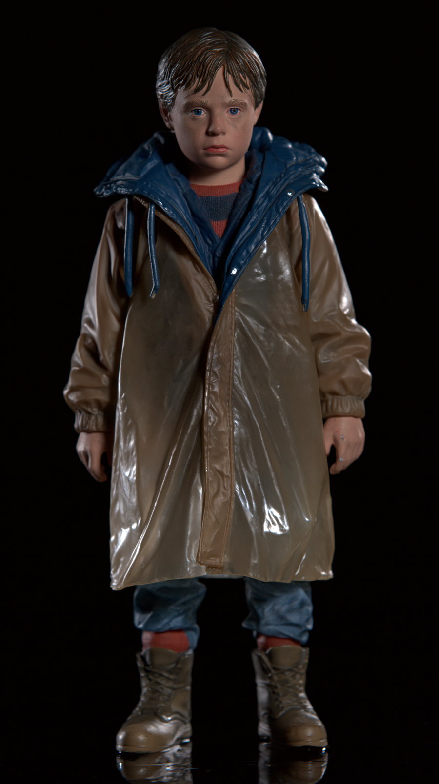 A highly detailed action figure of a young boy wearing a brown coat and blue hood, standing against a black background.