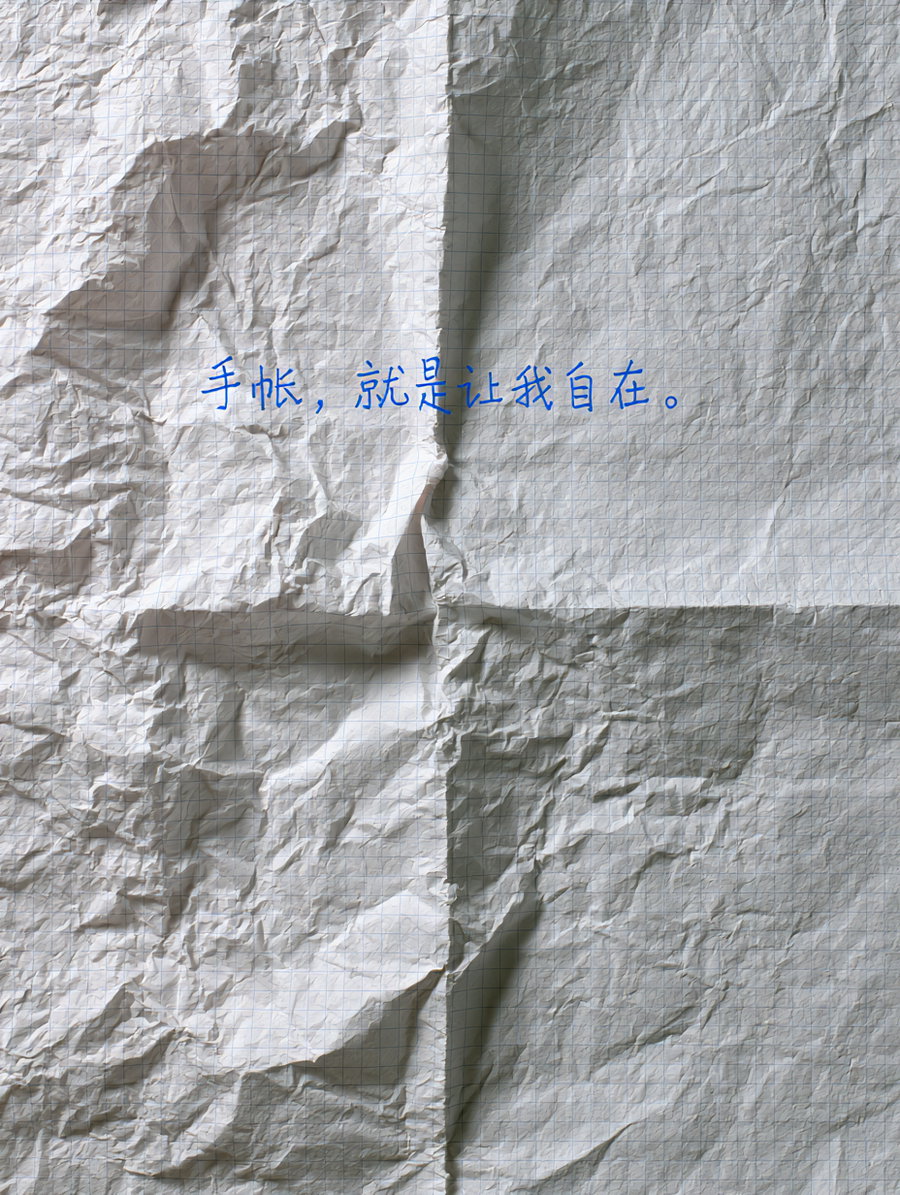 A crumpled off-white sheet of grid paper with visible wrinkles, displaying a handwritten blue Chinese slogan across the center creases.