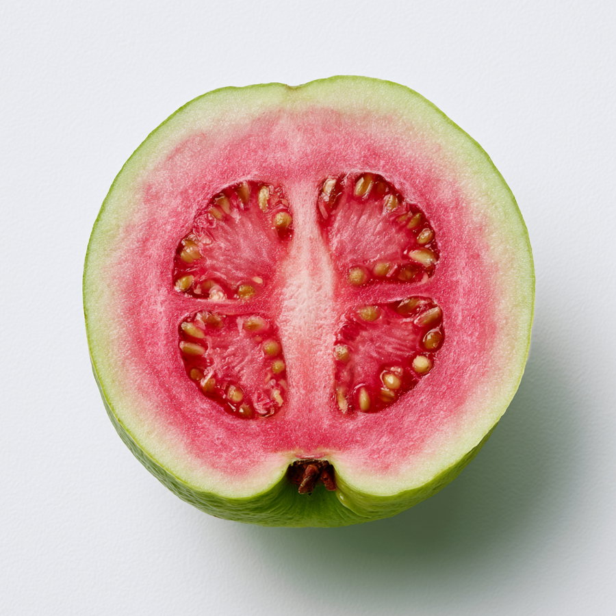 A sliced guava featuring pink flesh and green rind against a white background.