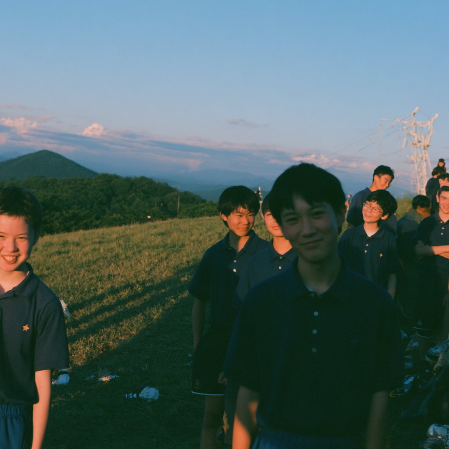 Group of elementary students wearing navy blue polo shirts, smiling outdoors during golden hour, with mountains in the background.