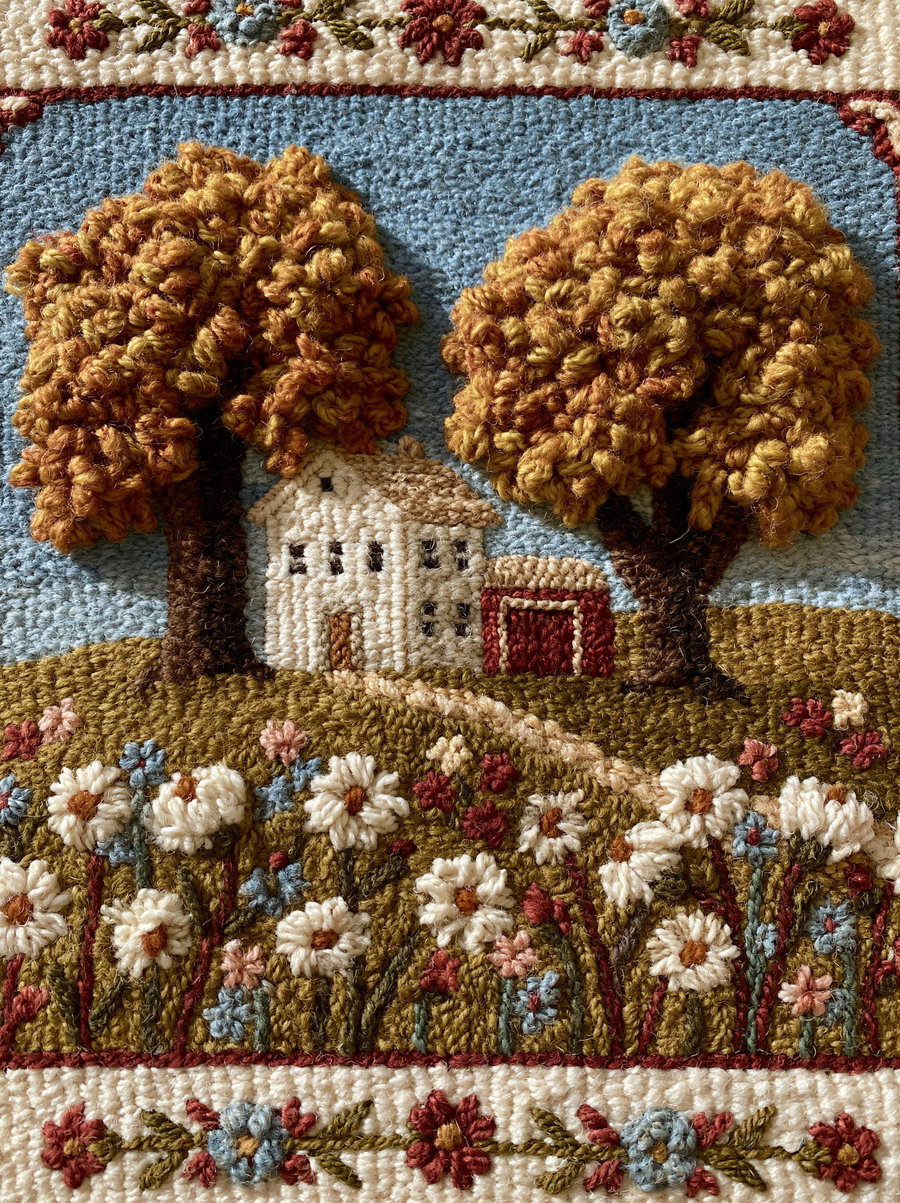 A handmade hooked wool rug featuring a white farmhouse, red barn, and large autumn trees amidst embroidered wildflowers, set against a bright blue sky.