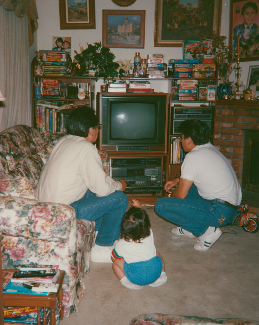 Family sitting on a floral couch in a cozy living room, watching a CRT television, with books and decorations around them.