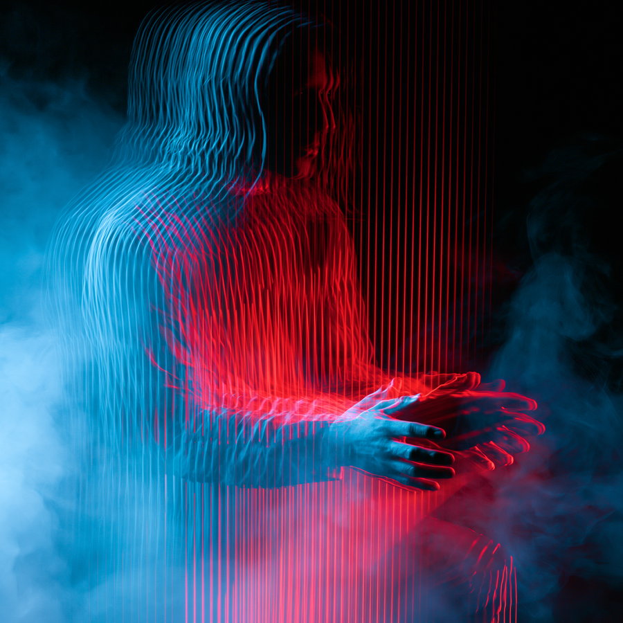 A blurred human figure dissolving into vertical laser light streaks, with hands and face slightly sharp against a dark background filled with neon red and blue lights and smoke.