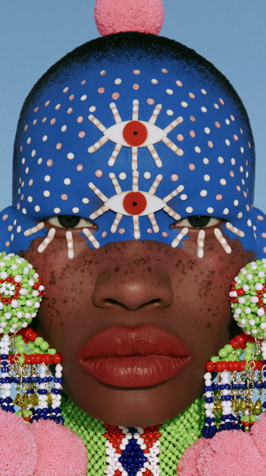 A close-up portrait of an African-American woman adorned with bright and quirky jewelry, featuring colorful patterns and face paint.