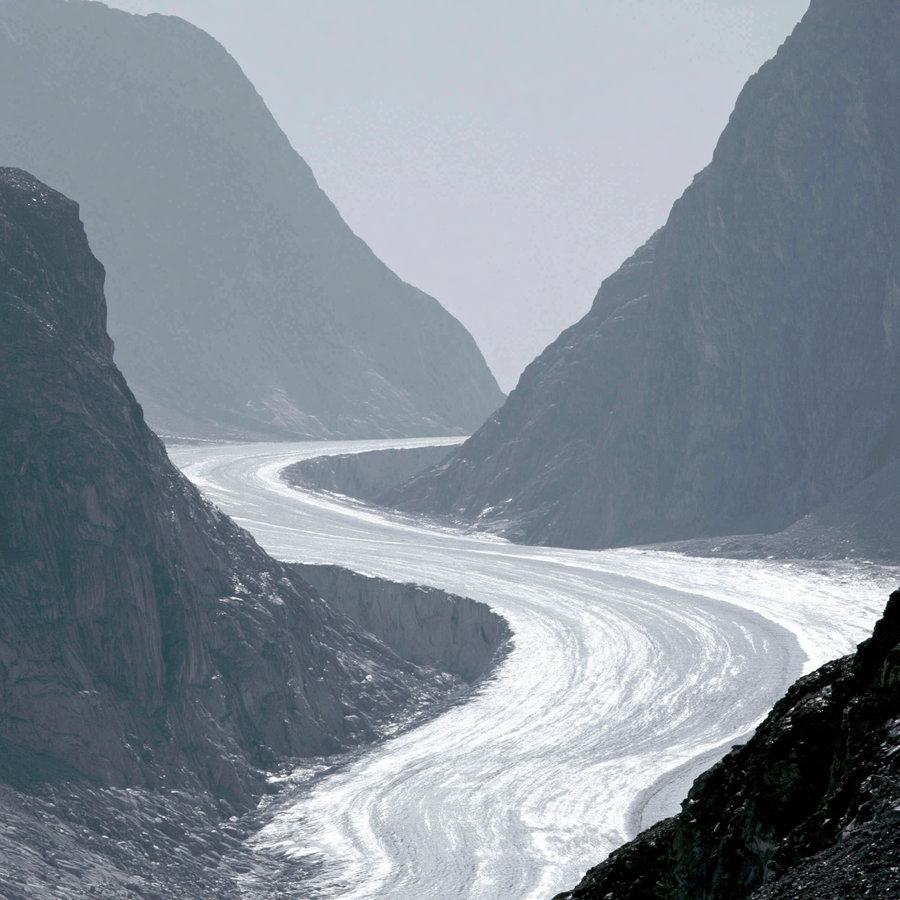 A winding glacier flowing through a narrow mountain valley, surrounded by steep rocky cliffs.