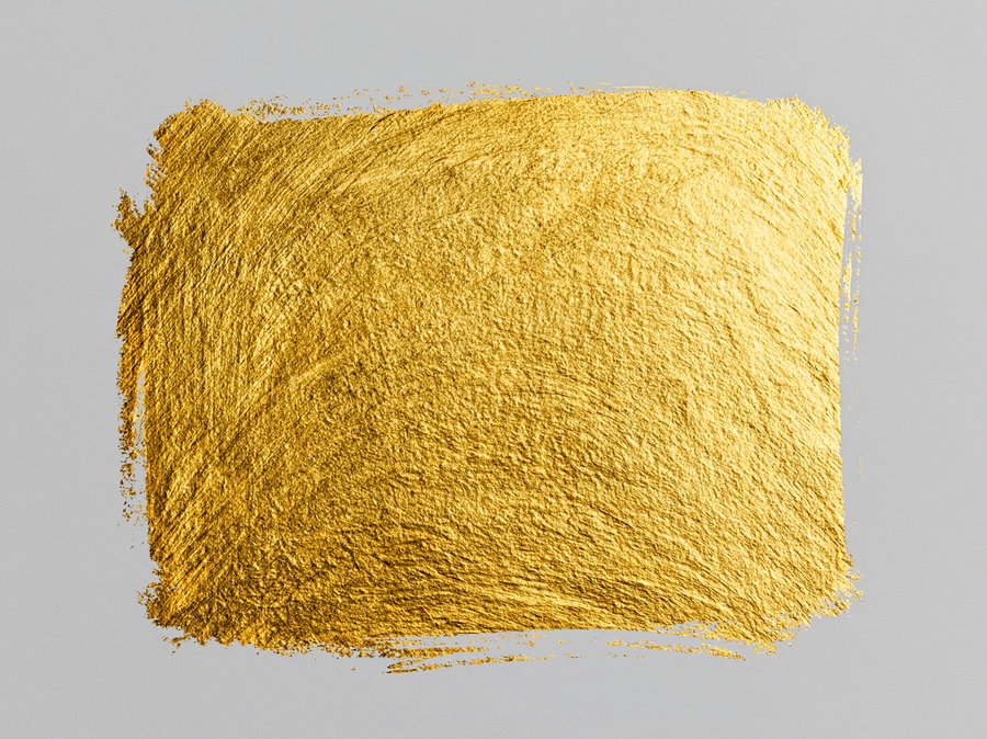 A textured square of gold paint swatch with visible brush strokes on a grey surface.