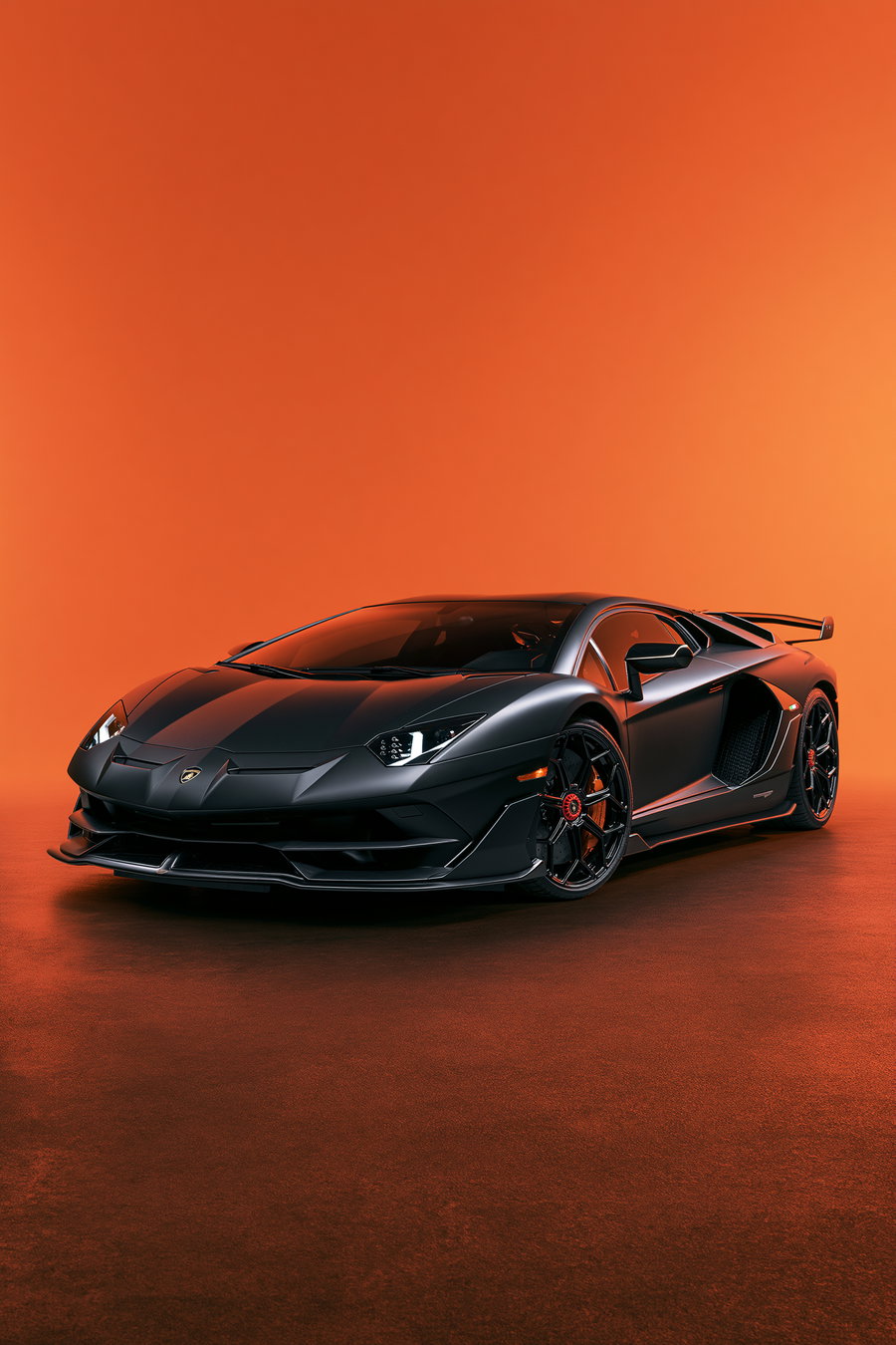 A Lamborghini Aventador SVJ in matte black paint positioned at a 3/4 front angle against a seamless vivid orange background with no reflections.
