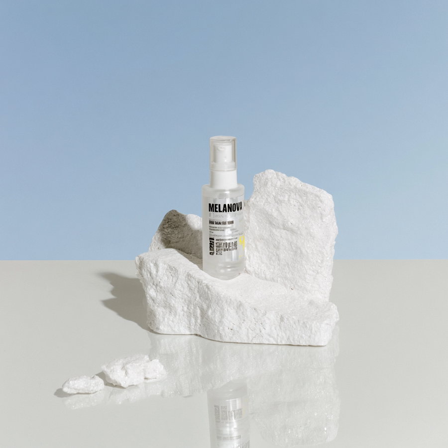 A clear serum bottle placed on a white marble surface, with a light reflection. The background is a clear blue sky illuminated by natural noon light, creating a high-end cosmetic photography vibe.