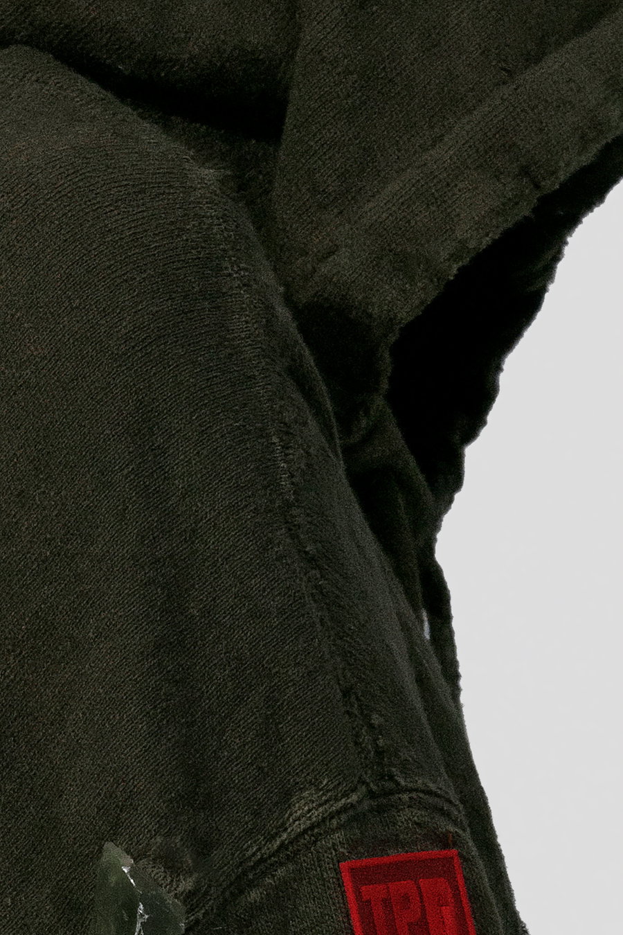 Close-up of a premium heavyweight hoodie in olive green with a translucent TPU badge on the sleeve.